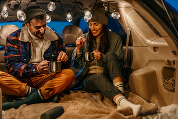 Couple sharing a peaceful moment with tea in their truck bed on a cold evening
