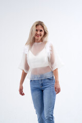 Obraz premium Blonde in a white T-shirt and blue jeans poses in a studio on a white background.