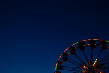 Illuminated Ferris wheel against a deep twilight blue sky; vibrant lights contrast beautifully with the dark background, creating a captivating night scene.