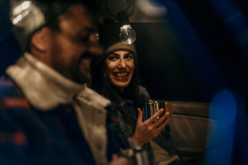 Cozy couple in a car trunk talking and sipping hot beverages on a chilly evening