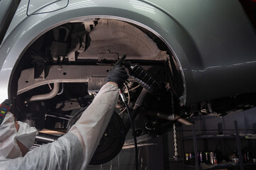 An auto mechanic applies anti-corrosion mastic to the underbody of a car.