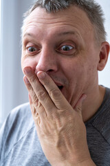 man wearing an orange hoodie with a wide-eyed surprised expression and raised hands, conveying shock or amazement.