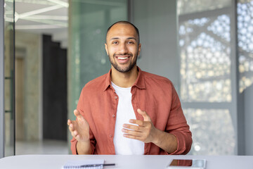 A confident, smiling professional sits at a desk, gesturing enthusiastically during a meeting in a...