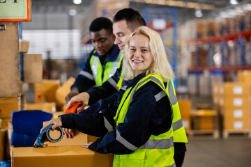 Female blonde hair professional worker wearing safety uniform using packing tape on packaging...