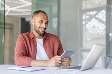 A smiling office worker interacts with a tablet and laptop in a contemporary workspace. The atmosphere is professional and innovative, highlighting the use of technology in a modern office setting.