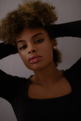 Fototapeta premium a close-up portrait of a person with curly hair, wearing a black top and an earring, in a dark and moody setting