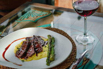 red wine sauce tenderloin served with smashed potatoes with onions and grilled asparagus, ready to eat at restaurant background with gşass of red wine