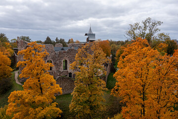 Naklejka premium Golden autumn foliage frames ancient stone ruins amid a cloudy sky.