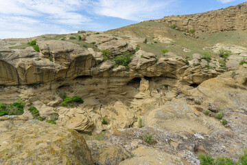 Sandstone cliffs covered with bushes and young grass. Blue sky with clouds and cliffs in the...