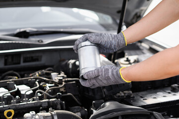 Auto mechanic holding fuel filter for diesel cars against background of car engine compartment. Man...