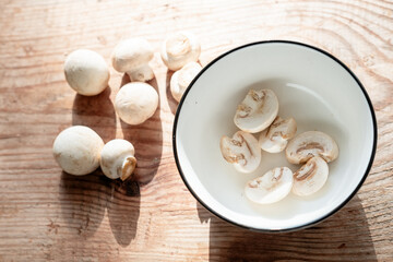 fresh, small champignons close-up and pieces in a bowl on a wooden background