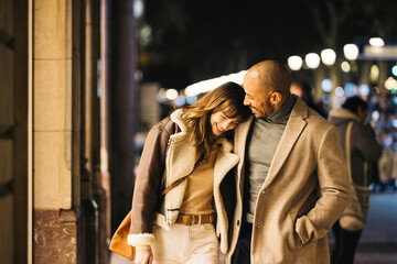A loving couple shares a joyful moment while strolling down a city street by night. They're enjoying a shopping excursion smiling and embracing intimately. © Jordi Salas