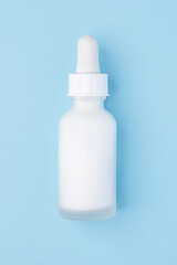 A frosted white dropper bottle with a minimalist design on a pastel blue background. Perfect for showcasing cosmetic products, branding, and packaging concepts