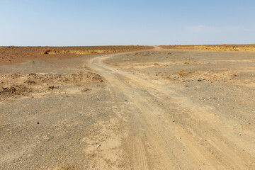 Dusty winding road through arid landscape under clear blue sky in remote area