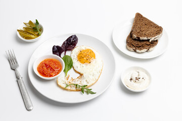 Fried egg on the plate, pickled cucumbers and bread,