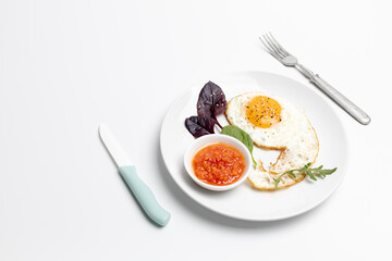 Fried egg and red sauce on the plate with the white background.