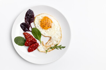 Fried egg, tomatoes and basil leaves on the plate.