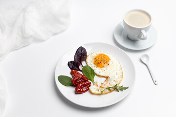 Fried egg, tomatoes and basil leaves on the plate.
