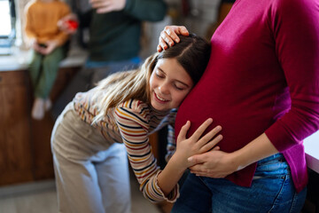 Daughter hugging, touching pregnant mother's belly. Little girl is looking at mom's belly with love