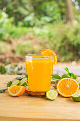 A glass of freshly squeezed orange juice on a wooden table surrounded by orange slices and orange leaves