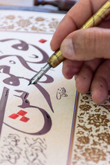 Close-up of a calligraphist writing an Arabic name for a customer in Arabic calligraphy with ink.
