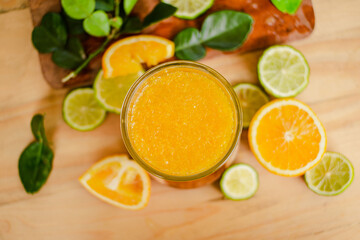 A glass of freshly squeezed orange juice on a wooden table surrounded by orange slices and orange leaves