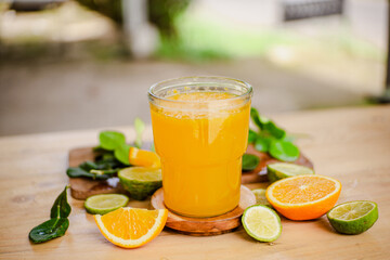 A glass of freshly squeezed orange juice on a wooden table surrounded by orange slices and orange leaves