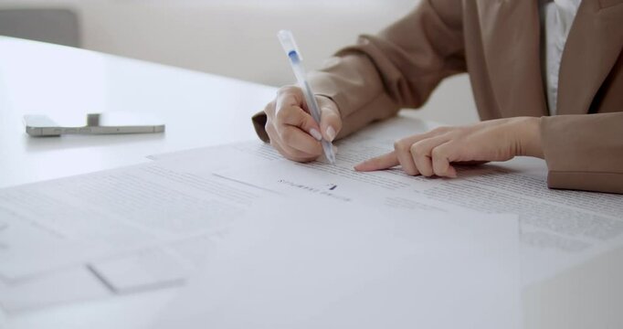 A focused office woman reviews and corrects spelling mistakes while checking sales data on a large stack of paper reports, ensuring accuracy and attention to detail in her work.