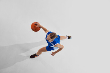 Top view image of competitive teen girl in blue uniform, basketball player during training session, in motion with ball against white studio background. Sport, youth, motion, healthy lifestyle concept © master1305