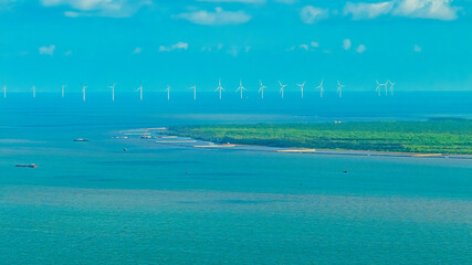 Tall windmill turbines against a clear blue sky, generating renewable energy in the serene Go Cong, Vietnam landscape by the sea. Like windmill park Westermeerdijk in the Noordoostpolder Netherlands.