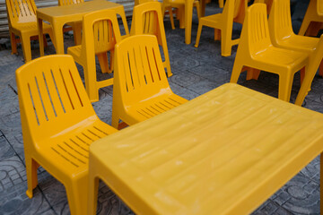 Bright yellow plastic chairs and tables arranged outdoors on patterned floor
