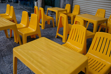 Bright yellow plastic tables and chairs arranged outdoors on a stone pavement