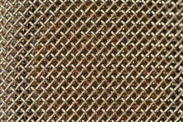 Macro view of a metallic mesh or grid. Mesh consists of interwoven metal wires forming a crisscross pattern, creating a textured and detailed surface. Microphone mesh background