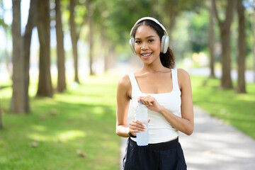 Beautiful African woman taking a break from her workout in a park, holding a bottle of water