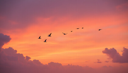 Fototapeta premium Flock of birds soaring through a vibrant sunset sky, with orange and pink hues blending into soft clouds