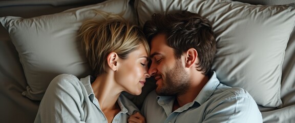 Obraz premium A tender moment unfolds as a couple lies closely together on a bed, their foreheads gently touching, radiating warmth and affection. The soft, muted colors of the bedding enhance the intimacy of the