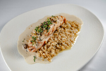 checken roll with mushroom white creamy sauce served on white plate and background, topped with herbs garnished with porridge