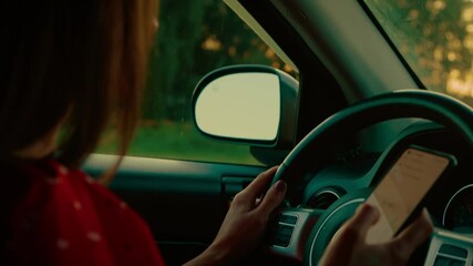 Woman using smartphone behind steering wheel at car, increasing risk of road accidents. Diverting attention from driving creates unsafe conditions for driver and others. Avoiding distractions is vital