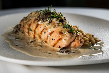 checken roll with mushroom white creamy sauce served on white plate and background, topped with herbs garnished with porridge