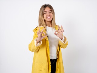 Beautiful teenager girl wearing yellow raincoat showing both hands with fingers in OK sign....