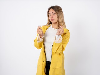 Beautiful teenager girl wearing yellow raincoat doing money gesture with hands, asking for salary payment, millionaire business