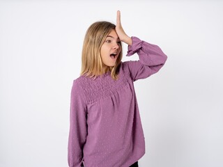Beautiful teenager girl wearing purple T-shirt surprised with hand on head for mistake, remember...