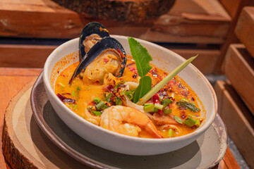 Spicy seafood soup with herbs in bowl, place on wooden slab. Thai dish called 