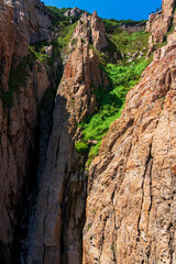 Majestic Rocky Cliff Surrounded by Lush Greenery Under Bright Blue Sky