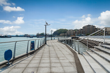 Obraz premium Scenic Waterfront Walkway with Clear Blue Skies and Urban Background
