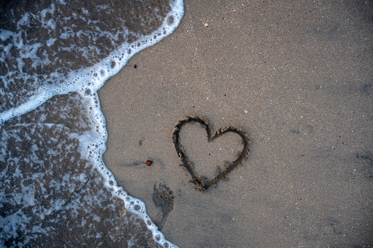 A heart is drawn on the sand on the beach at sunset. Romantic sunset on the beach. Heart shape. Heart symbol. Love. - Powered by Adobe