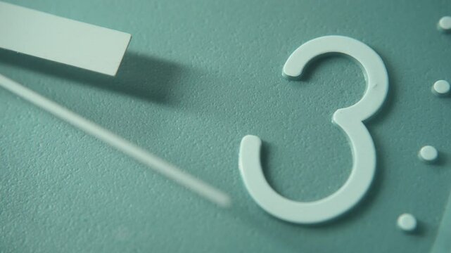 Close-up shot of number 3 on a blue wall clock with moving second hand. The time is three o'clock.