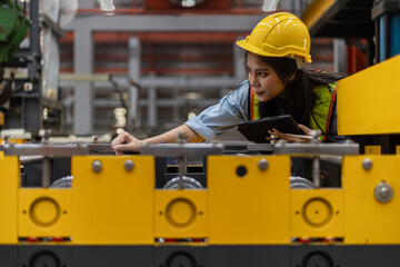 Female mechanical engineer in safety suit checking or inspecting a machine in metal sheet production system. Using technology for iron sheet formation and shape. Young factory worker examining machine