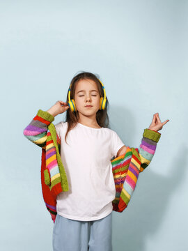 A serene young girl wearing yellow headphones and a colorful striped cardigan listens to music with her eyes closed. Her relaxed pose and peaceful expression evoke a sense of calm and enjoyment.
