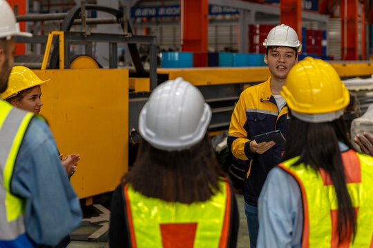 A young foreman gives instruction and job description for the day to his mechanical engineer team next to the iron steel machine. Cooperation among factory workers. Safety brief before the day starts